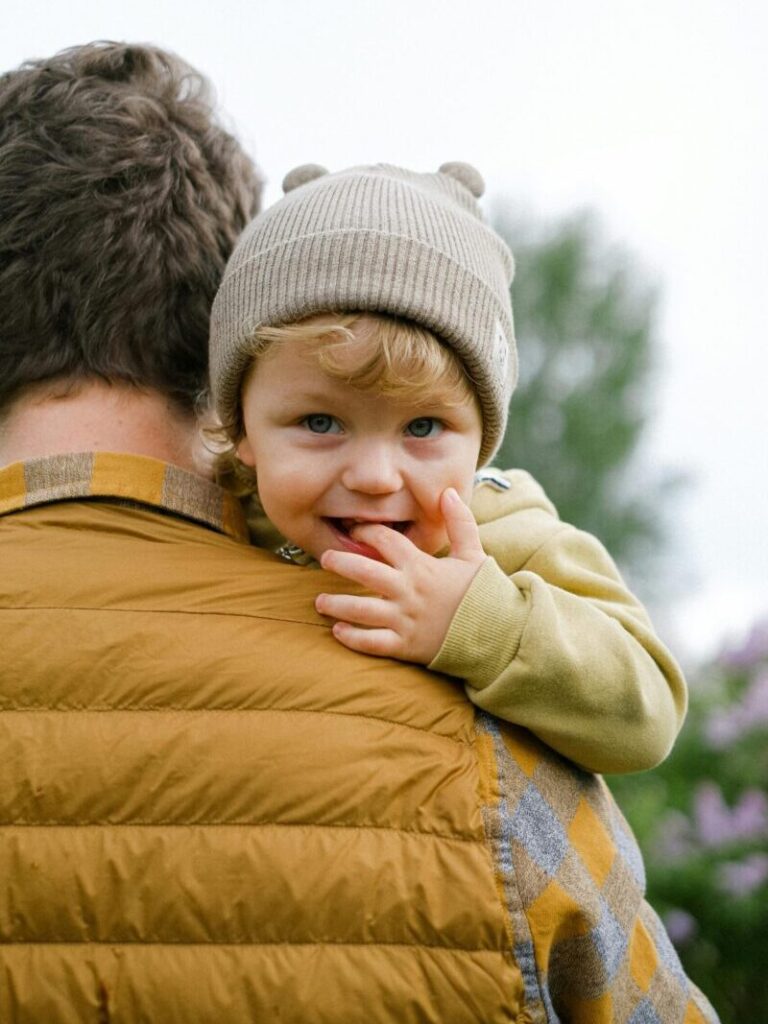 A father carries his smiling child with beanie in a winter landscape.